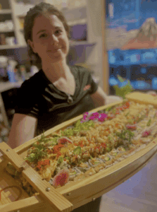 Server holding a large sushi boat at Sushiyama restaurant, filled with various rolls and garnishes.